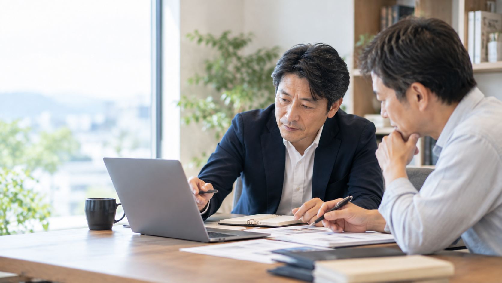 窓辺のテーブルで資料を囲み、一緒に検討する打ち合わせ